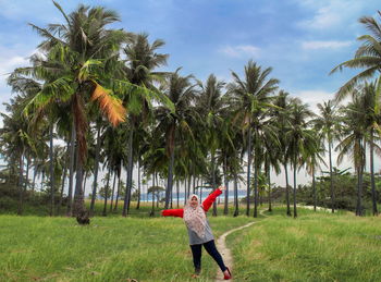 Full length of man standing by palm trees on field against sky