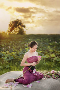 Woman holding water lily while sitting on plastic sack