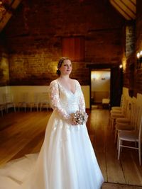 Young woman looking away in wedding dress standing against wall