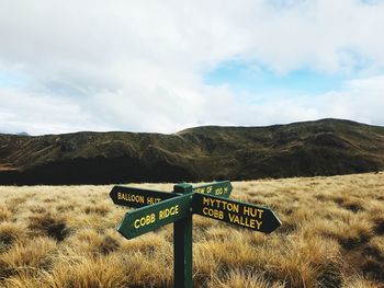 Road sign on field against sky