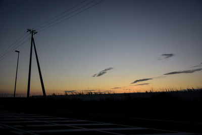 Silhouette electricity pylons against sky during sunset