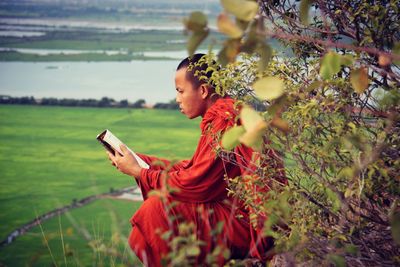 Side view of monk reading book on field