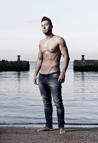 Full length of shirtless man standing on sea shore against sky