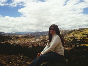 Portrait of smiling woman sitting on mountain against sky