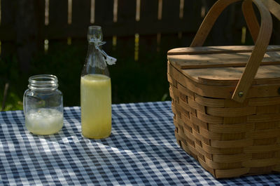 Vintage picnic basket, blue checked table cloth, bottles of lemonade and drinking jar glasses