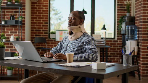 Businessman with neck brass using laptop in office