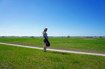 Full length of woman standing on field against clear blue sky