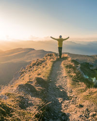 Rear view of man standing on cliff against sky