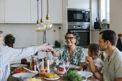 Smiling senior woman passing bowl to man while sitting at dining table at home
