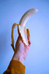 Close-up of hand holding banana against blue background