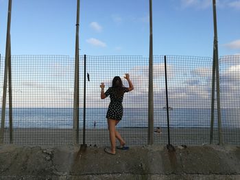 Rear view of woman looking at sea through fence 