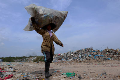 Low angle view of woman carrying garbage on head against sky