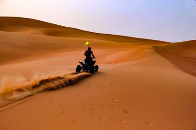 Man riding motorcycle on desert against clear sky