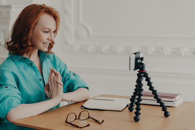 Smiling woman podcasting on smart phone at table