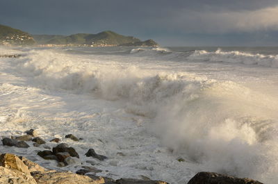 Waves breaking on rocks at beach against sky