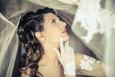 Beautiful bride sitting amidst veil at home