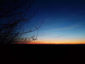 Silhouette bare trees on landscape against sky at sunset