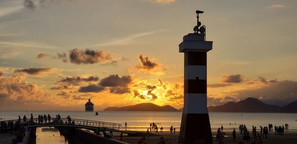 Lighthouse by sea against sky during sunset