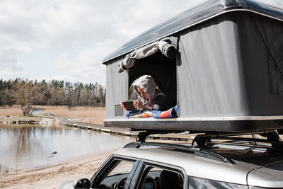 Boy sitting in a roof top tent playing nintendo whilst camping