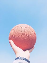 Cropped hand holding basketball against clear sky