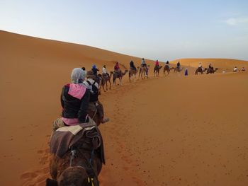 Rear view of people riding in desert against clear sky