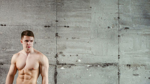 Close-up of shirtless muscular man standing by wall