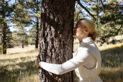 Side view of woman standing by tree trunk