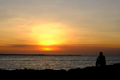 Silhouette man looking at sea against sky during sunset