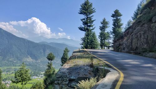 Road amidst trees and mountains against sky