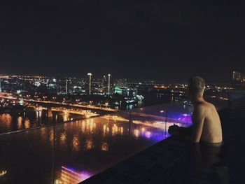 Rear view of shirtless man and illuminated cityscape against clear sky at night