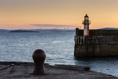 Lighthouse by sea against sky during sunset