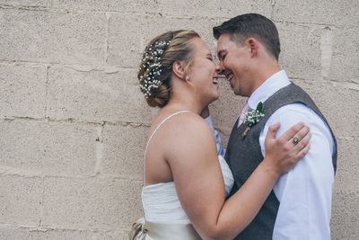 Side view of bride and groom laughing face to face against stone wall