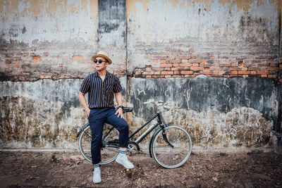 Portrait of young man leaning on bicycle against wall