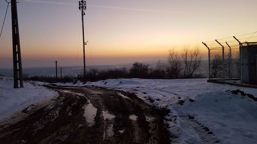 Snow covered landscape against sky during sunset