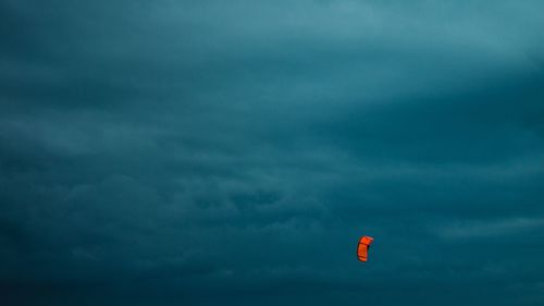 Low angle view of orange parachute flying in cloudy sky