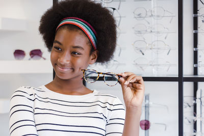 Happy young woman african american afro hair smile and holding glasses standing at in optical shop.