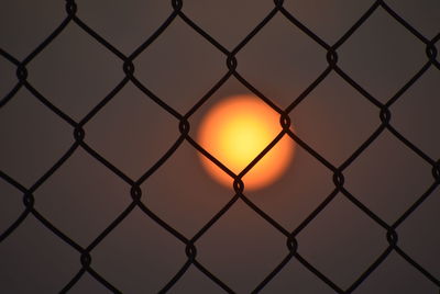 Full frame shot of chainlink fence against sun in sky during sunset