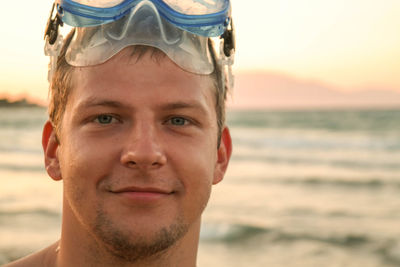 Close-up portrait of young man with scuba mask at beach during sunset