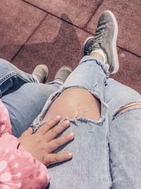 Low section of mother and daughter sitting against footpath