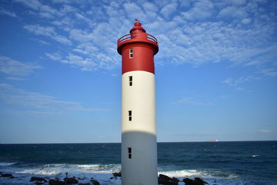 Lighthouse by sea against blue sky