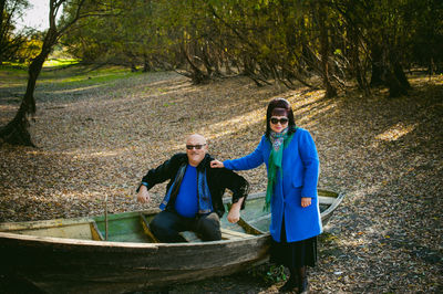 Mature woman standing by man sitting in boat at forest during autumn