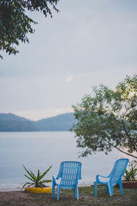 Empty chairs and table by sea against sky