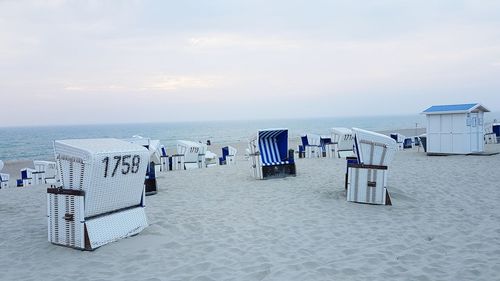 Hooded chairs on beach against sky