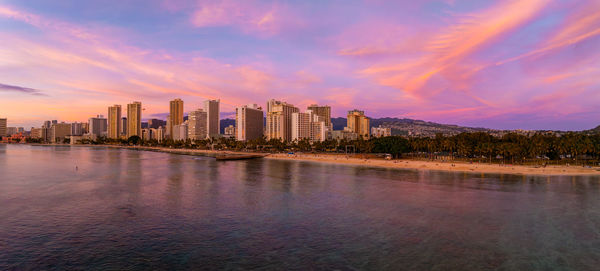 Buildings by river against sky during sunset