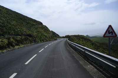 Road passing through country landscape against cloudy sky