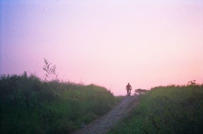 Rear view of man cycling on hill against sky during sunset