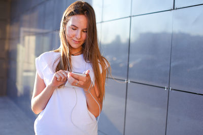 Smiling young woman using mobile phone on street