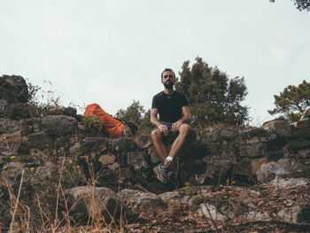 Young man on rock against sky