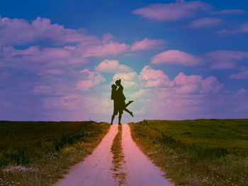 Rear view of man walking on road amidst field against sky