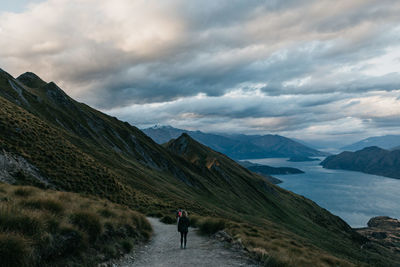 Rear view of woman walking on mountain road against sky